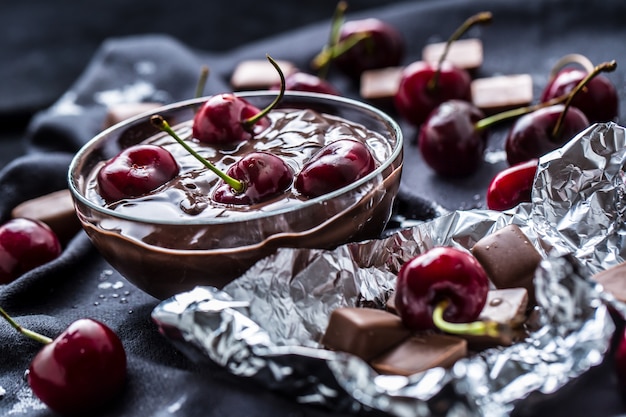 Ciliegie fresche in ciotola con cioccolato sulla tovaglia scura.