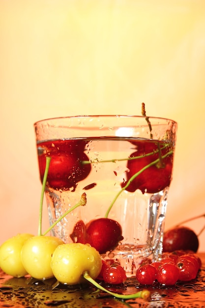 Ciliegie in un bicchiere su uno sfondo tonico Un mazzo di ciliegie mature fresche che cadono in un bicchiere d'acqua con le bolle closeup Cocktail rinfrescante concept