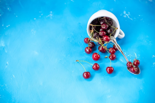 Ciliegie mature e succose in tazza di ceramica bianca, ciliegia rossa, frutta biologica, cibo estivo, primo piano, isolato su sfondo blu Ciliegie fresche. Bacche estive Copi lo spazio Ciliegia matura sparsa