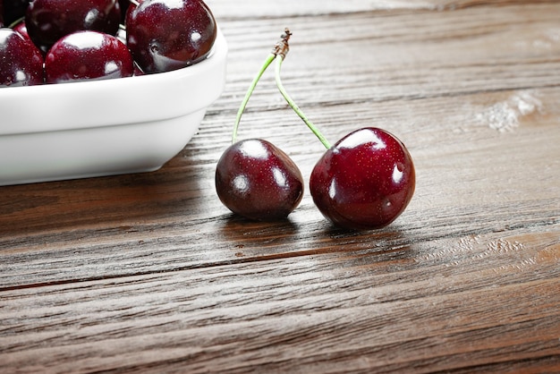 Ciliegie succose mature fresche rosse in un piatto bianco e due frutti su un fondo di legno