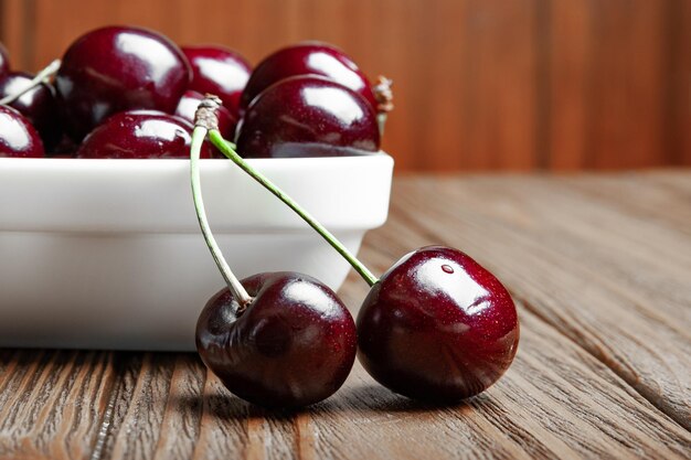 Ciliegie succose mature fresche rosse in un piatto bianco e due frutti su un fondo di legno