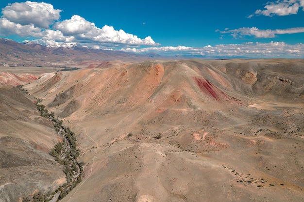 Cime montuose multicolori con molti alberi si estendono in lontananza sotto un cielo azzurro con diverse nuvole.