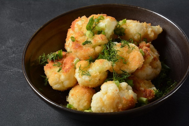 Cimette di cavolfiore fritto in pastella su un piatto nero Cavolfiore fritto ricoperto