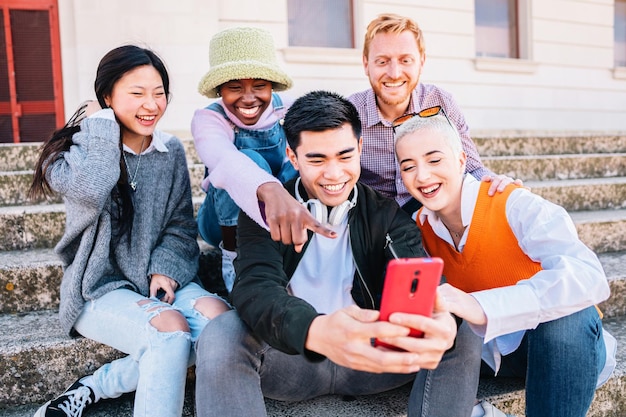 Cinque giovani amici seduti all'aperto e guardando il cellulare Gruppo di persone che guardano video