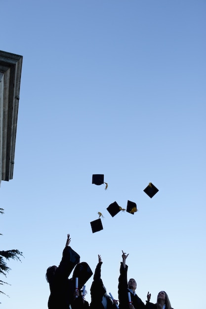 Cinque studenti laureati che gettano il cappello in cielo