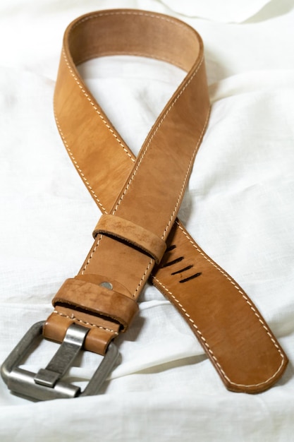 Cintura beige in vera pelle spessa su fondo bianco in tessuto di lino Produzione di cinture fatte a mano con materiali naturali ecocompatibili