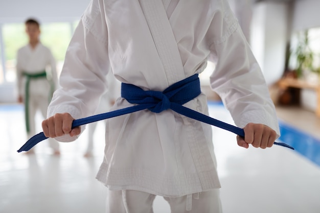 Cintura blu. Primo piano di una ragazza che indossa un kimono bianco che si allaccia la cintura blu prima di praticare l'aikido