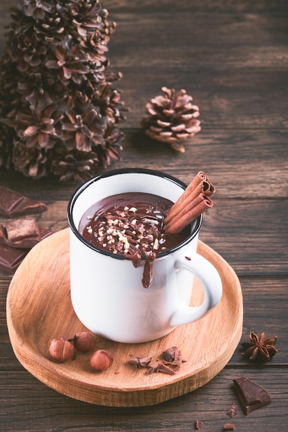 Cioccolata calda Cioccolata calda piccante fatta in casa con nocciola tritata alla cannella in tazza smaltata su fondo di legno vecchio Accoglienti vacanze stagionali