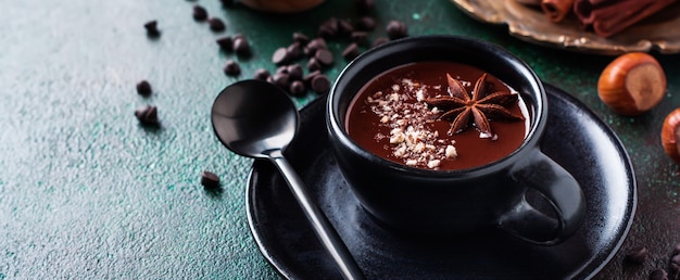 Cioccolata calda con anice e noci in tazza di ceramica nera sul vecchio sfondo di cemento verde scuro. Messa a fuoco selettiva.