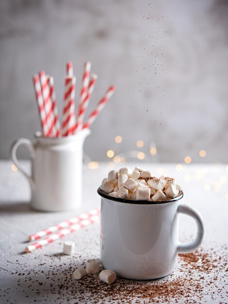 Cioccolata calda con marshmallow e un tubo di carta rossa su un tavolo grigio