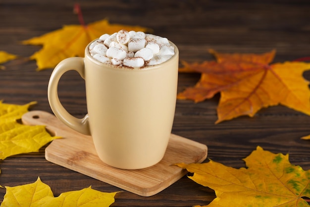 Cioccolata calda con marshmallow in una tazza su un tavolo di legno sullo sfondo delle foglie autunnali