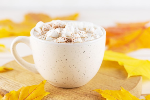 Cioccolata calda con marshmallow su una tavola di legno su uno sfondo di foglie autunnali