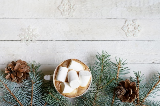 Cioccolata calda di Natale con marshmelow su fondo di legno bianco, rami di albero di Natale che decorano, spazio della copia