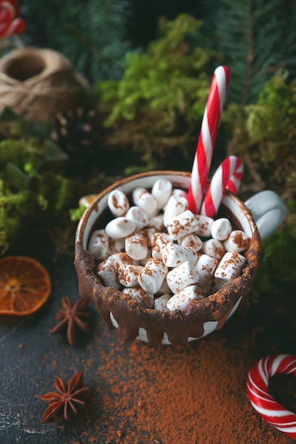 Cioccolata calda di Natale in una tazza nera con arance caramellate, rami di abete e bastoncino di zucchero su sfondo scuro, messa a fuoco selettiva