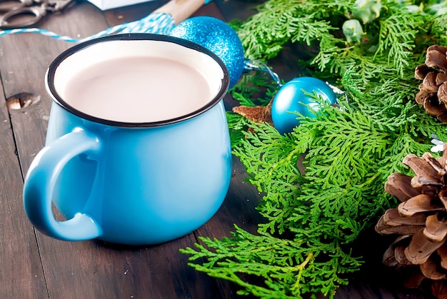 Cioccolata calda in tazza blu sul tavolo in legno scuro con decorazioni natalizie, regali, pigne