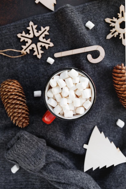 Cioccolata calda in una tazza rossa con marshmallow circondato da decorazioni natalizie su un maglione di lana