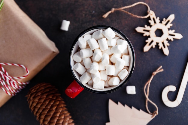 Cioccolata calda in una tazza rossa con marshmallow circondato da decorazioni natalizie