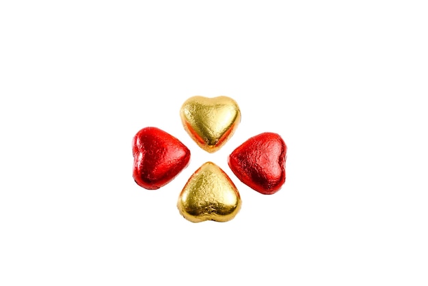 Cioccolatini a forma di cuore avvolti in un foglio rosso e giallo oro su sfondo bianco