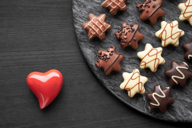 Cioccolatini a forma di stella su superficie scura strutturata con heari in ceramica rossa