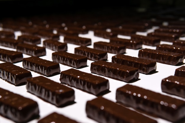 Cioccolatini appena versati con cioccolato liquido su un nastro trasportatore di un primo piano di una fabbrica di dolciumi