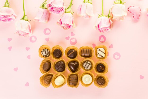 Cioccolatini assortiti con rose rosa su sfondo rosa.