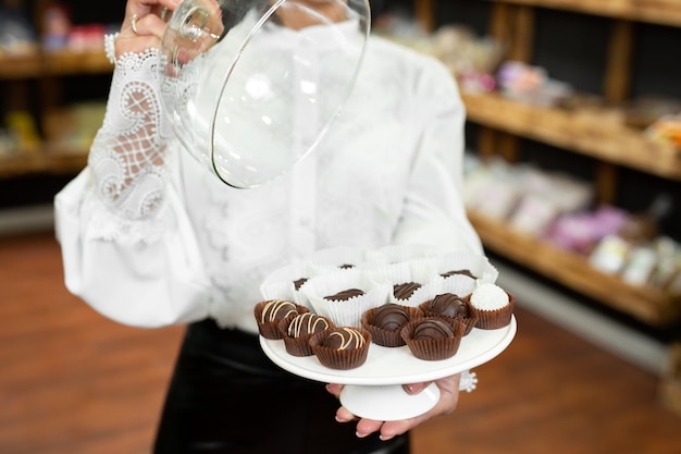 Cioccolatini fatti a mano su un vassoio sotto un coperchio di vetro nelle mani di una giovane e bella donna nel negozio