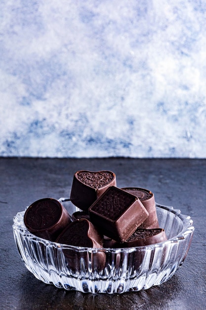 Cioccolatini su vassoio in vetro intagliato, fotografati su sfondo scuro.