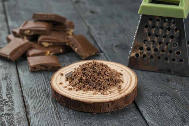 Cioccolato grattugiato su un supporto di legno sullo sfondo di una grattugia e cioccolato intero