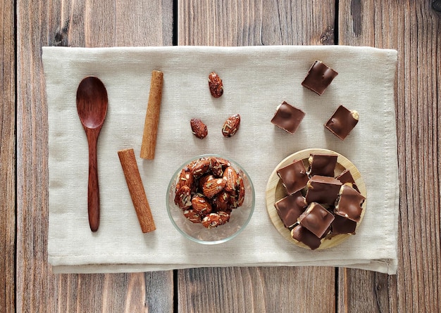 Cioccolato, mandorle speziate, bastoncini di cannella, cucchiaio di legno su fondo di legno. Vista dall'alto, distesa.