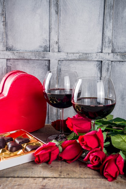 Cioccolato, rose, bicchieri di vino e scatola del cuore sul tavolo di legno