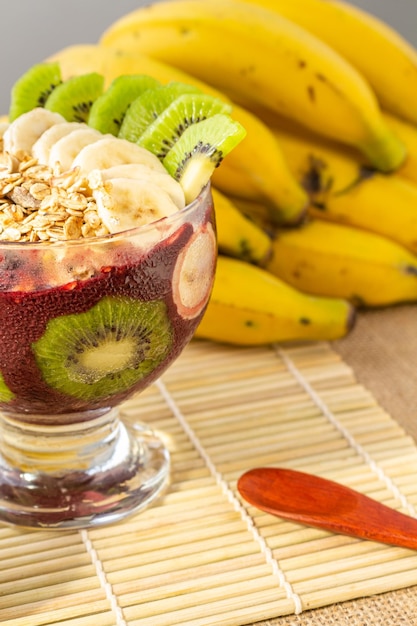 Ciotola Acai con fiocchi di kiwi, banana e avena su un tavolo con decorazioni tropicali.