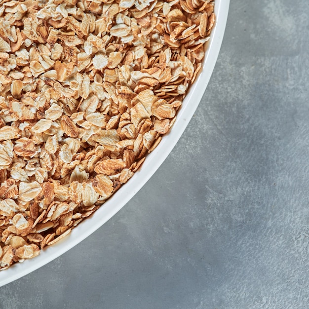 Ciotola bianca del primo piano con i fiocchi d'avena asciutti per la preparazione del porridge sano su un fondo di pietra grigia