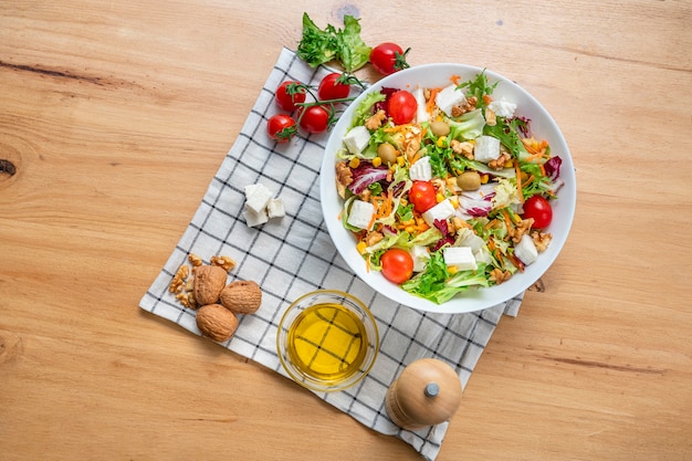 Ciotola bianca di insalata vegetariana con lattuga iceberg con un mix di ingredienti sani come noci, pomodorini, noci, carote, formaggio fresco e mais. Vista dall'alto