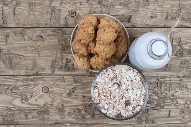 Ciotola con biscotti fatti in casa, bottiglia di latte e muesli sulla tavola di legno marrone.