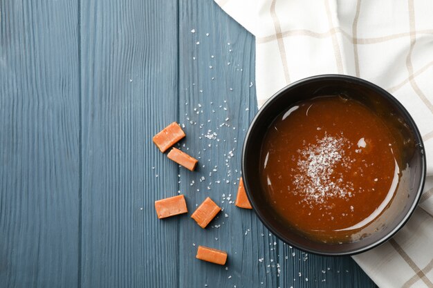 Ciotola con caramello salato e caramelle su spazio in legno, spazio per il testo