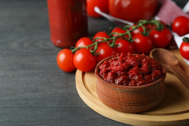 Ciotola con concentrato di pomodoro sul tavolo di legno scuro con ingredienti