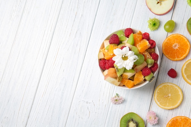 Ciotola con deliziosa insalata e frutta a fette su un tavolo di legno chiaro