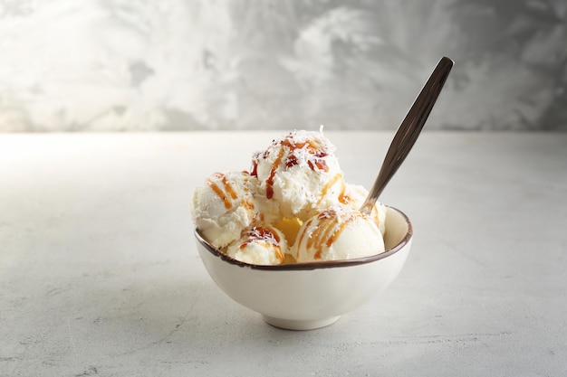 Ciotola con palline di gelato al cocco e sciroppo di caramello su sfondo chiaro