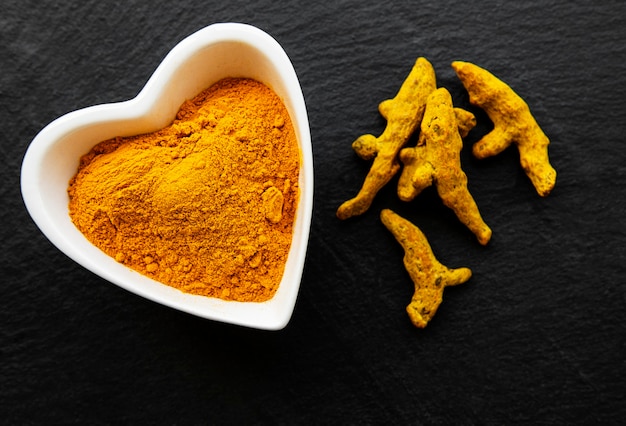 Ciotola con polvere di curcuma e radici secche su una superficie di cemento nero