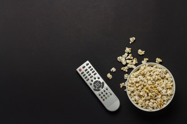 Ciotola con popcorn e telecomando TV su uno sfondo nero. Il concetto di guardare la TV, film, serie TV, sport, spettacoli. Vista piana, vista dall'alto.