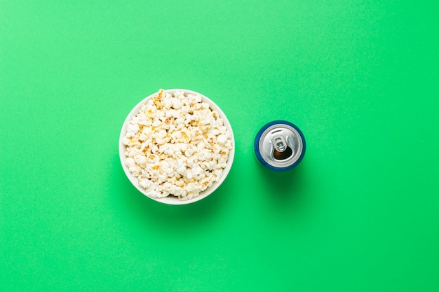 Ciotola con popcorn e una lattina di bevanda su uno sfondo verde. Il concetto di guardare film e programmi TV preferiti, competizioni sportive. Vista piana, vista dall'alto.