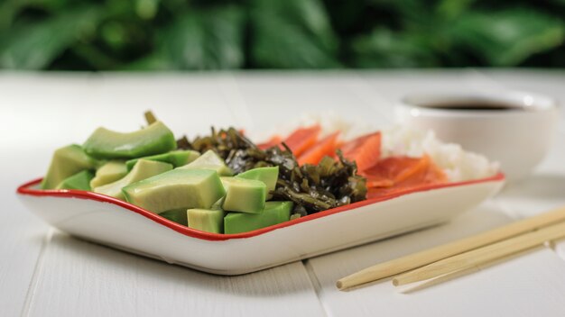 Ciotola con riso, avocado, salmone e fuco su una tavola di legno bianca contro un albero verde.