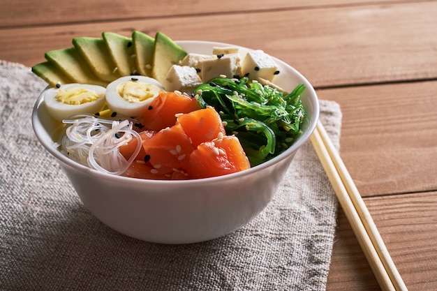 Ciotola con salmone, avocado, tovaglia di lino sul fondo in legno