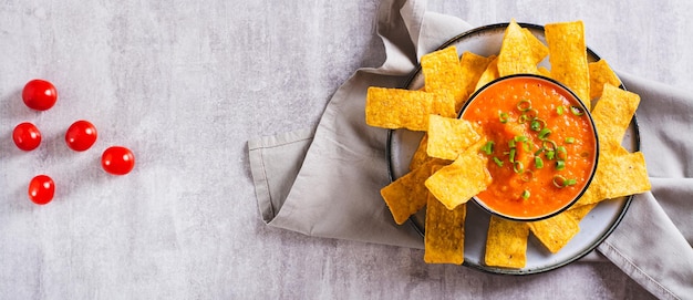 Ciotola con salsa di pomodoro messicana e patatine di mais sul banner web con vista dall'alto del tavolo