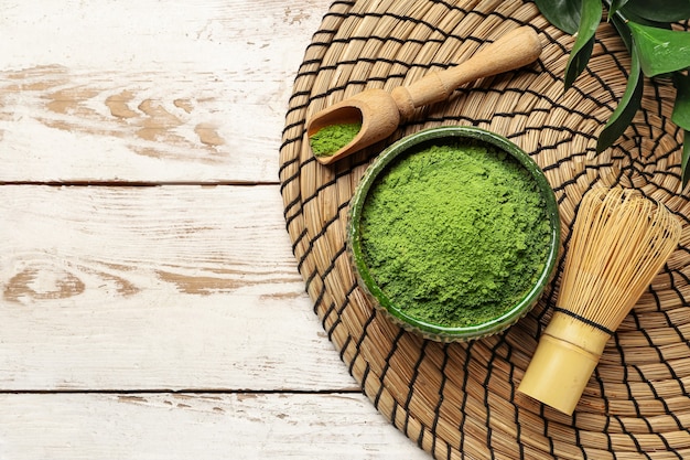 Ciotola con tè matcha in polvere, cucchiaio e chasen su fondo in legno chiaro