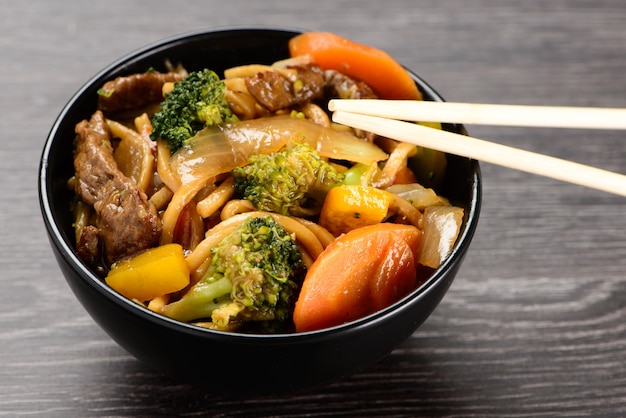 Ciotola con yakisoba e hashi su sfondo nero