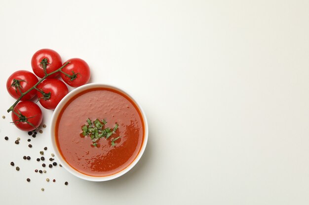 Ciotola con zuppa di pomodoro e ingredienti su bianco