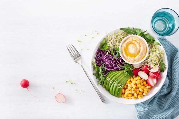 Ciotola da pranzo vegana con avocado e mais con hummus, cavolo rosso, ravanello e germogli