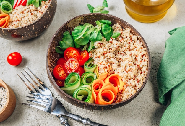 Ciotola del Buddha vegano Pasto sano quinoa pomodoro cetriolo carota ravanello insalata di mais in ciotole di cocco su sfondo concreto Messa a fuoco selettiva