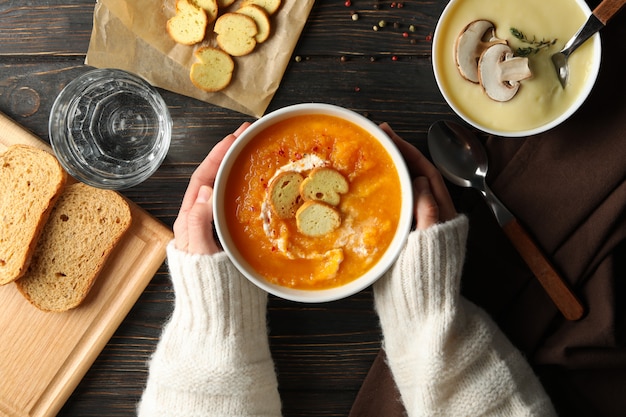 Ciotola della tenuta della donna con la minestra crema della zucca sulla vista di legno e superiore